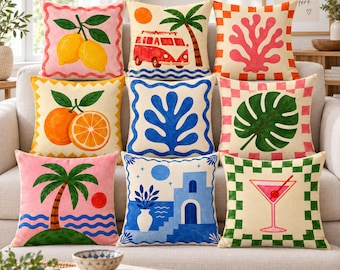May include: A collection of nine square throw pillows featuring colorful graphic prints including lemons, a red van, coral, oranges, blue abstract shapes, a monstera leaf, a palm tree, a Mediterranean coastal scene, and a cocktail glass.