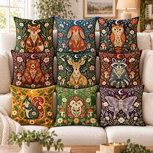 Puede incluir: Una colección de nueve cojines cuadrados dispuestos en un sofá, cada uno con una ilustración distinta de un animal del bosque, incluyendo un zorro, conejo, búho, oso, ciervo, mapache, ardilla, erizo y polilla, rodeados de motivos florales.