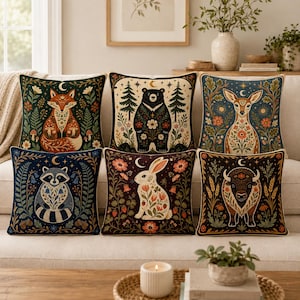 Peut inclure: Un ensemble de six coussins carrés présentant des illustrations détaillées d'un renard, d'un ours, d'un cerf, d'un raton laveur, d'un lapin et d'un bison. Chaque coussin affiche un animal des bois entouré d'éléments botaniques et célestes.