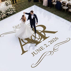 May include: A couple dances on a white dance floor with gold lettering and the date "June 2, 2026." The floor features the initials "A&R" in a decorative font. The bride wears a white wedding dress, and the groom wears a dark suit.