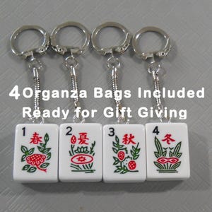 May include: Four Mahjong tile keychains with silver keyrings. Each white tile features a different red and green design and a number from 1 to 4. The text "4 Organza Bags Included Ready for Gift Giving" is above the keychains.