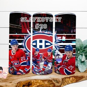 Könnte beinhalten: Ein zylindrischer Becher mit einem Eishockeyspieler in einem rot-weiß-blauen Trikot mit der Nummer 20. Das Design umfasst den Text SLAFKOVSKY #20, ein großes Logo der Montreal Canadiens und ein Bild einer Eishockeyarena mit Eisfläche.