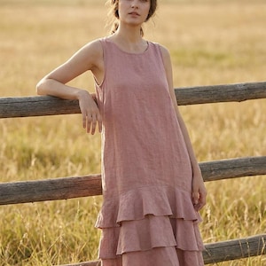 May include: A sleeveless knee-length dress in a dusty rose color. The garment features a round neckline and a tiered skirt design with three distinct horizontal ruffles starting from the mid-thigh area, creating a layered and textured appearance.