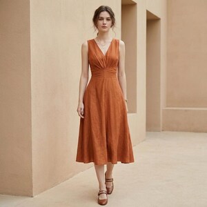 May include: A sleeveless midi dress in a solid burnt orange color featuring a deep V-neckline, a fitted bodice with subtle vertical pleating at the waist, and a flared A-line skirt that falls below the knees, paired with brown leather sandals.