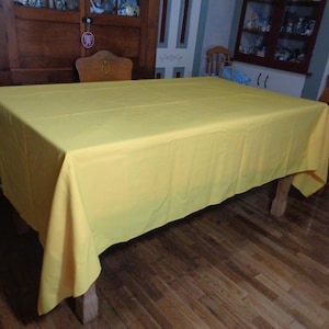May include: A bright yellow tablecloth covers a wooden table in a dining room. The tablecloth is smooth and wrinkle-free, with a slight sheen.