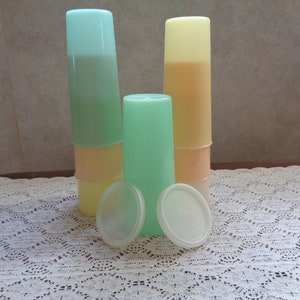 May include: Stack of three clear plastic cups with lids. The cups are in shades of green, yellow, and orange. The lids are white.