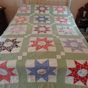 May include: A green and white quilt with a star pattern. Each star is made of different fabrics and has a name embroidered in the center. The quilt is made with a variety of fabrics, including floral prints, polka dots, and geometric patterns.