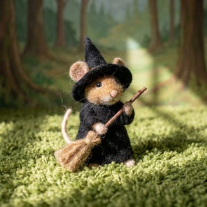 Puede incluir: Una figura de ratón de color canela hecha con fieltro de aguja, que lleva un sombrero de bruja negro puntiagudo y un vestido negro a juego. El ratón tiene orejas pequeñas y redondas, ojos de cuentas negras y sostiene una escoba.