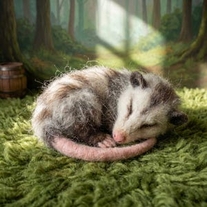 May include: A needle-felted opossum figurine curled into a ball, featuring textured white and brown fur, dark ears, a pink nose, and a long, smooth pink tail. The creature is resting on a textured green surface with a forest backdrop.