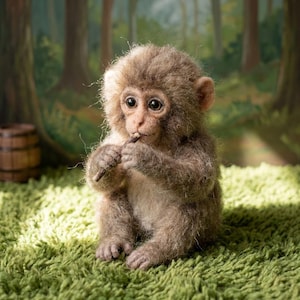 May include: A needle-felted monkey figurine with textured brown and tan fur, large dark eyes, and small ears. The monkey is sitting in an upright position, holding a small dark brown twig near its mouth with both hands, showcasing detailed craftsmanship.