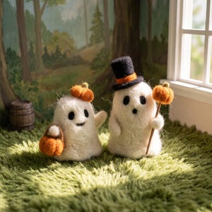 Può includere: Due statuette di fantasmi in lana infeltrita bianca. Un fantasma indossa un cilindro nero con una fascia arancione e tiene una piccola zucca arancione su un bastoncino. L'altro ha una piccola zucca arancione sulla testa e porta un cestino.