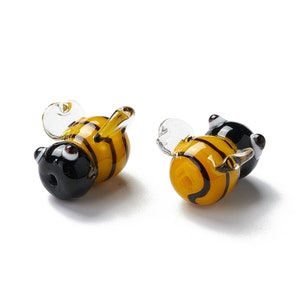 May include: Two glass bee charms with black and yellow stripes. The bees have clear wings and black eyes.