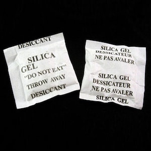 May include: Two white silica gel packets with black text. The text on the packets reads "Desiccant Silica Gel "Do Not Eat" Throw Away Desiccant" and "Silica Gel Desicateur Ne Pas Avaler Silica Gel Desicateur Ne Pas Avaler Silica Gel".