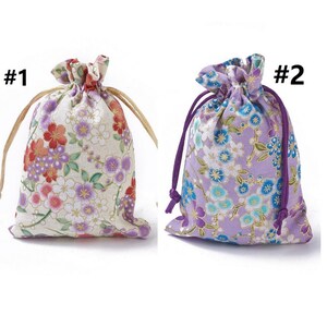 May include: Two drawstring bags with floral patterns. The bag on the left is white with pink and purple flowers. The bag on the right is purple with blue and white flowers. Both bags have purple drawstrings.