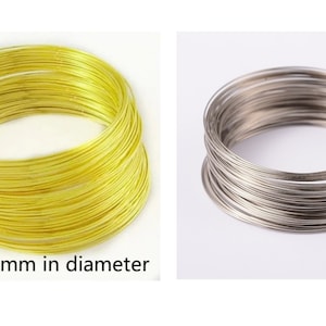 May include: Two stacks of thin, round, metal wire. The stack on the left is gold and the stack on the right is silver. Both stacks are about 65mm in diameter.  about 65mm in diameter