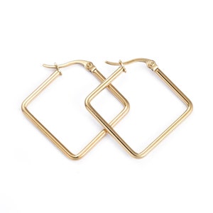 May include: A pair of gold square hoop earrings. The earrings are made of a thick, smooth metal and have a simple, modern design.