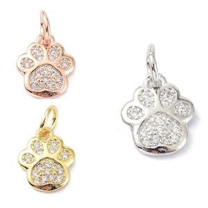 May include: Three silver charm pendants in the shape of a paw print with clear sparkling rhinestones. The charms are on a white background.