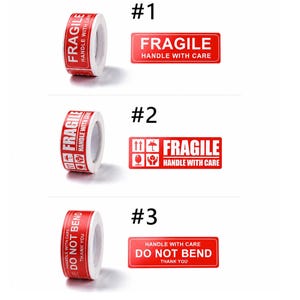 以下が含まれることがあります： 赤と白の粘着式配送ラベルのロール3種。ロール#1には「FRAGILE HANDLE WITH CARE」の文字。ロール#2には「FRAGILE HANDLE WITH CARE」の文字と、矢印、傘、グラス、箱のアイコン。ロール#3には「DO NOT BEND」と記載されています。