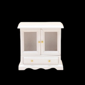 May include: A miniature white wooden cabinet with two glass doors and a drawer. It features gold-coloured knobs and a decorative, scalloped base. The cabinet's top has a gentle curve.