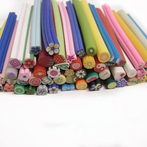 May include: A collection of colourful polymer clay sticks with various designs, including flowers, fruits, and geometric shapes. These sticks are used for nail art and crafting.