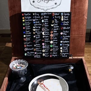 May include: A wooden box containing a black display board with the text Joyside Magic and a list of items with corresponding small charms. Below, a clear glass bowl filled with small trinkets, a white ceramic bowl, and a small lantern.