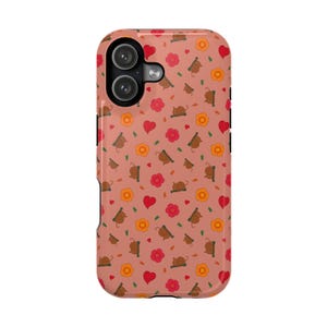 May include: A phone case with a dusty rose background featuring a repeating pattern of small brown capybaras, orange flowers, red flowers, and red hearts. The case has a black camera cutout area in the upper left corner with two circular lenses.