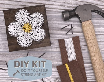 May include: DIY string art kit with a white flower design on a wooden base. The kit includes white and yellow string, nails, and a hammer.