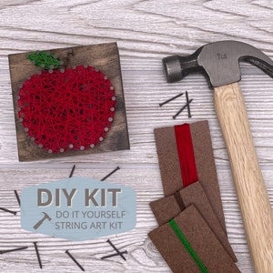 May include: DIY string art kit with a red apple design. The kit includes a wooden base, red string, nails, and a hammer.  The kit also includes instructions for creating the string art.