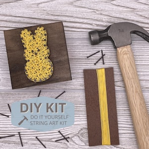 May include: DIY string art kit with a yellow bunny design on a wooden base. The kit includes a hammer, nails, and yellow string.