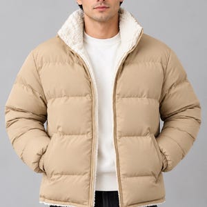 Könnte beinhalten: Eine beige Steppjacke mit hohem Kragen, durchgehendem Frontreißverschluss und weißem Sherpa-Fleece-Futter. Die Jacke verfügt über horizontale Steppnähte, lange Ärmel mit elastischen Bündchen und zwei seitliche Eingrifftaschen.