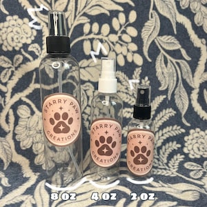 Könnte beinhalten: Drei durchsichtige Sprühflaschen aus Kunststoff mit schwarzen oder weißen Pumpverschlüssen. Jede Flasche hat ein rundes Etikett mit dem Text Starry Paw Creations und einem Pfotenabdruck. Die Flaschen sind mit 8 oz, 4 oz und 2 oz beschriftet.