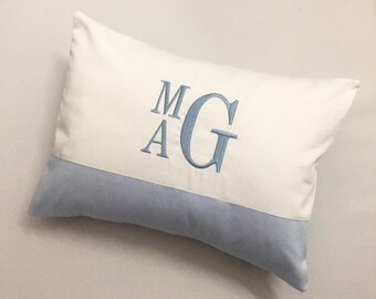 May include: A white pillow with a blue embroidered monogram "MAG" on the front. The pillow has a light blue bottom edge.
