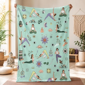 May include: A light mint green throw blanket featuring a repeating pattern of people in various yoga poses, cats, lotus flowers, dreamcatchers, suns, moons, eyes, and Om symbols. The illustrations are rendered in a soft, colourful, and detailed style.