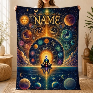 May include: A rectangular blanket featuring a dark blue celestial design with the word NAME in gold lettering. The print displays a central meditating figure, a large zodiac wheel, various moons, planets, and stars in vibrant gold and blue tones.