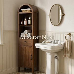 May include: A tall, arched wooden bathroom storage cabinet with open shelving, a single drawer, and a lower cabinet door. The unit features a dark wood finish and is positioned next to a white pedestal sink with a brass faucet and oval mirror.