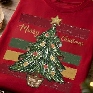 Peut inclure: Un t-shirt rouge avec un motif de sapin de Noël vert décoré de boules colorées et d'une étoile dorée. Le texte Merry Christmas est imprimé en lettres dorées sur des bandes horizontales de couleur rouge foncé, verte et dorée.