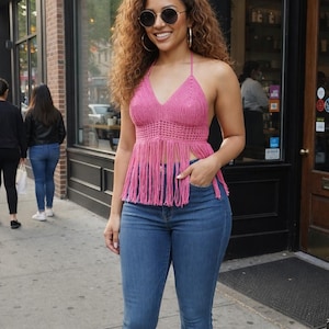 Puede incluir: Top halter rosa de ganchillo con flecos y vaqueros azules. El top tiene cuello en V y se combina con vaqueros acampanados. La mujer lleva gafas de sol y pendientes de aro.