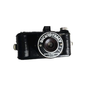 Könnte beinhalten: Eine schwarze Vintage-Kamera von Dick Tracy mit strukturiertem Gehäuse. Das kreisförmige Objektivgehäuse trägt den Text Dick Tracy, Seymore Products Co. Chicago, Made in U.S.A. und Inst. Time. Eine kleine Gesichtsillustration ist oben zentriert.