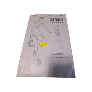 Op de afbeelding: Een vintage Superior Pattern naaipatroon-envelop voor een jurk, maat 14, buste 32. De witte papieren hoes bevat een zwarte lijntekening van een persoon in een jurk met korte mouwen die een tennisracket vasthoudt, met tekst waaronder Sears Roebuck and Co.