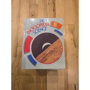 May include: A hardcover Funk & Wagnalls New Encyclopedia of Science book, volume 15. The light gray cover features a circular graphic showing a crescent moon over a textured brown landscape, with red and blue accents and bold text.