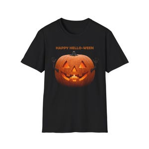 Könnte beinhalten: Ein schwarzes T-Shirt mit kurzen Ärmeln und einer Grafik eines geschnitzten orangefarbenen Kürbisses mit einer brennenden Kerze im Inneren. Der Kürbis hat kleine schwarze Arme, die erhoben sind, und der Text HAPPY HELLO-WEEN steht in Orange darüber.