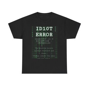 Op de afbeelding: Een zwart t-shirt met korte mouwen en een grafische print met een groene binaire code achtergrond. De tekst luidt ID10T ERROR, IDENTITY-10-T EXCEPTION - UNHANDLED, The problem exists between keyboard and chair. Please reboot the user and try again.
