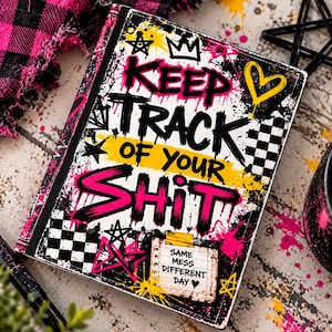 Puede incluir: Un cuaderno rectangular con cubierta blanca que presenta salpicaduras de pintura estilo grafiti en negro, rosa y amarillo. El texto dice KEEP TRACK OF YOUR SHIT en letras negras y rosas, con una nota SAME MESS DIFFERENT DAY.