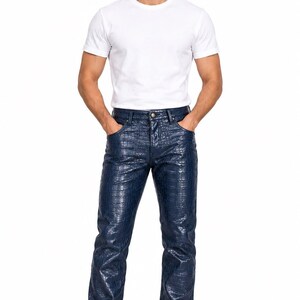 Peut inclure: Un t-shirt blanc uni à manches courtes et col rond associé à un pantalon bleu foncé doté d'une texture brillante en relief façon peau de crocodile. Le pantalon présente une coupe classique à cinq poches avec fermeture à bouton et baskets blanches.