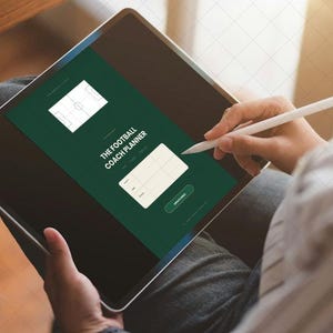 Puede incluir: Una tableta digital que muestra una interfaz verde oscuro titulada THE FOOTBALL COACH PLANNER, con un diagrama de campo de fútbol blanco, una tabla de cuadrícula para notas y un botón, interactuando con un lápiz óptico blanco.