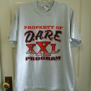 May include: A gray t-shirt with the text "PROPERTY OF DARE XXL PROGRAM" printed in black and red letters.