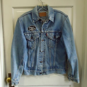 May include: A light blue denim jacket with a black patch that says "Indian 24/7" on the left chest.