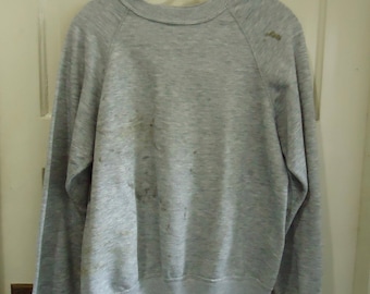 May include: A gray sweatshirt with a crew neck and long sleeves. The sweatshirt has a faded look and some stains.