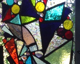 May include: A stained glass window with a geometric design featuring various colours, including red, blue, green, yellow, and purple. The glass pieces are arranged in a random pattern, creating a modern and abstract look.