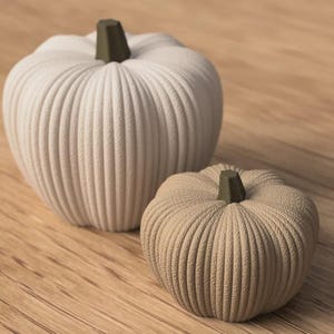 May include: Two decorative pumpkins with a textured, ribbed surface. The larger pumpkin is off-white, and the smaller pumpkin is a light tan color. Both pumpkins feature a dark olive green stem at the top, creating a simple and clean appearance.